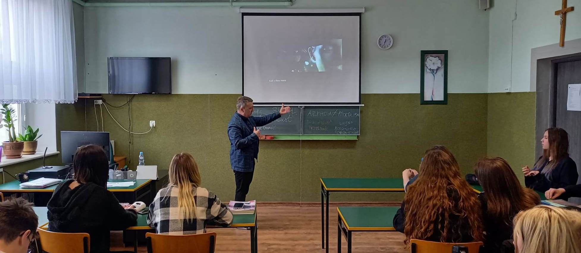 dr Pliszka w trakcie prowadzenia wykładu stoi przy tablicy na której wyświetlany jest film