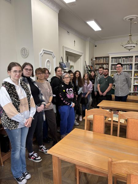 studenci pozują do zdjęcia z bibliotekarzem i dr Prachnio na tle regału z książkami